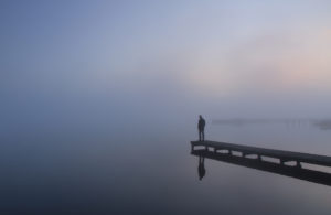 A man in quiet prayer standing alone on a pier on a foggy morning