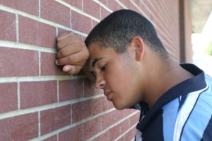 Man leaning against a brick wall looking anguished