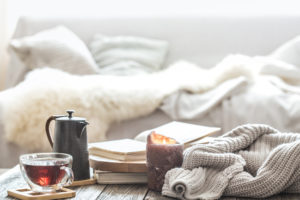 A living room with a cup of tea, a burning candle and a knitted sweater showing comfort