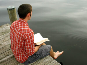 a young man sitting on a dock reading the Bible